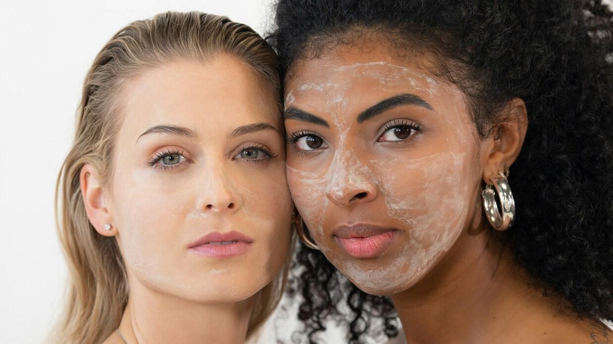 Zwei Frauen mit unterschiedlichen Hautpflegeprodukten auf dem Gesicht, nah beieinander vor einem weißen Hintergrund.