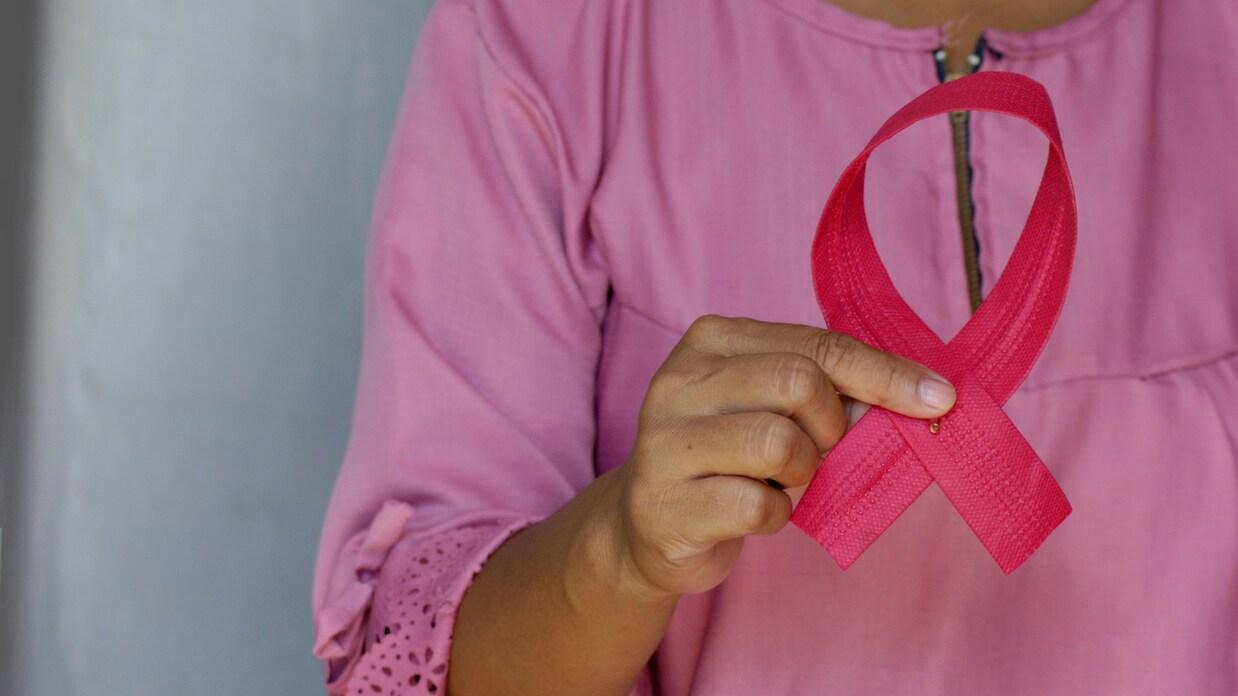 Nahaufnahme einer Person, die ein pinkes Schleifenband in der Hand hält, getragen in einem schlichten rosa Oberteil.